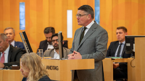 Mann im Anzug hält Rede an Rednerpult.