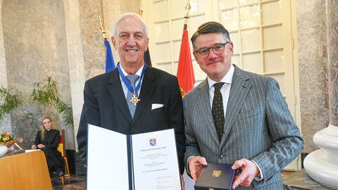 Zwei Männer stehen nebeneinander und halten eine Urkunde hoch.