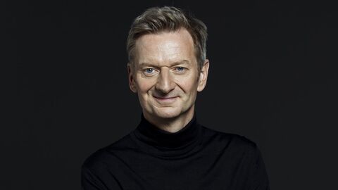 Ein Mann schaut frontal in die Kamera. Der Hintergrund und seine Kleidung sind komplett schwarz.