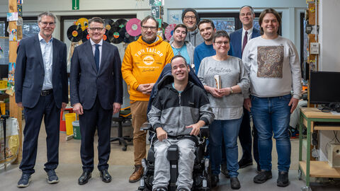 Mehrere Menschen schauen in Kamera. Eine Person sitzt im Rollstuhl