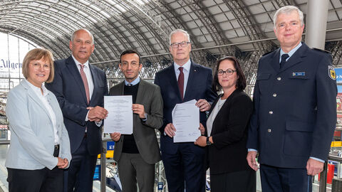 Innenminister Poseck steht mit weiteren Personen im Frankfurter Hauptbahnhof und hält Schreibstücke in die Kamera