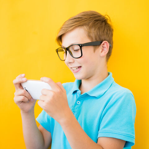 Junge vor einer gelben Wand schaut lachend auf sein Smartphone